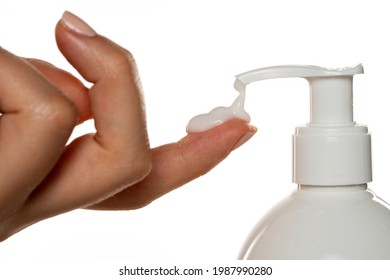 A Bottle Of Cosmetic Product With A Pump Throws The Cream On A Woman's Finger On A White Background