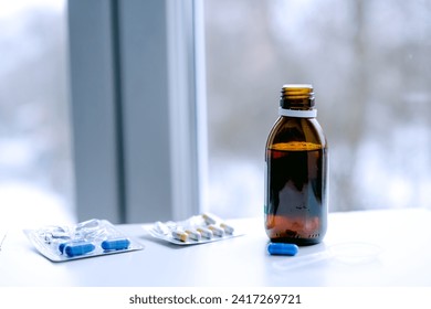 Bottle of cough syrup and different pills. Blurred winter landscape outside the window. Cope spacy.