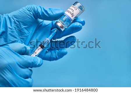 A bottle of COVID-19 Sputnik V vaccine and a syringe with an injection needle against coronavirus infection in the doctor's hand in a nitrile glove on a blue background. Close-up. Place to copy. The