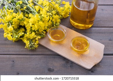 bottle and cups with rapeseed oil, next to young rapeseed flowers on a wooden table