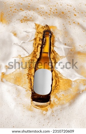 Bottle of delicious lager beer diving into foam of beer, splashes. Creative image for ad. Concept of alcohol drink, taste, vacation, holiday, brewery. Poster, flyer
