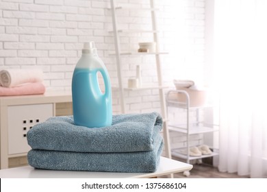 Bottle of detergent and clean towels on table indoors, space for text. Laundry day