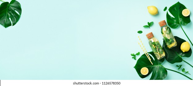 Bottle of detox water with mint, lemon and tropical monstera leaves on blue background. Flat lay. Banner. Citrus lemonade. Summer fruit infused water. Top view with copy space - Shutterstock ID 1126578350