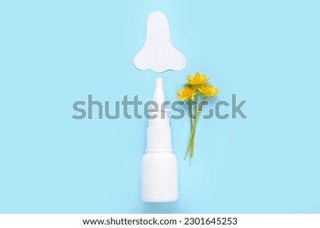 Bottle of drops with paper nose and flowers on blue background. Seasonal allergy concept