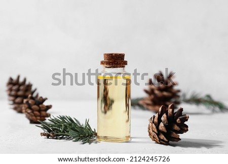 Bottle of essential oil, fir branch and pine cones on light background