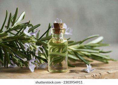 A bottle of essential oil with fresh blooming rosemary twigs on a wooden table