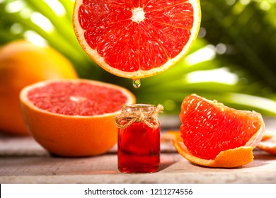 Bottle of essential oil from grapefruits on wooden table and green leaves background - alternative medicine