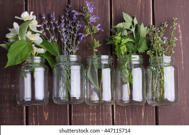 Bottle Of Essential Oil With Herbs Oregano, Sage, Camomile, Lavander, Parsley, Thyme And Mint Set Up On Old Wooden Background.