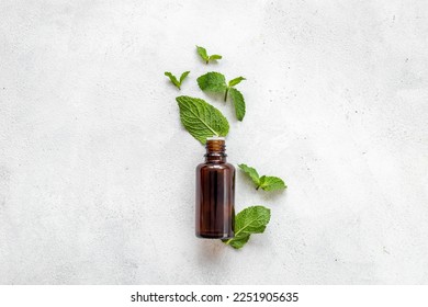 Bottle of essential peppermint oil with fresh green mint leaves.