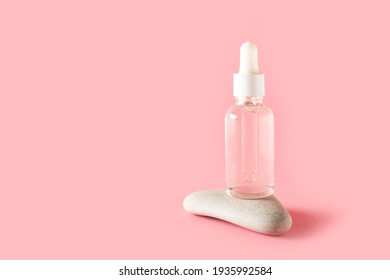 Bottle of facial serum on stone on pink background, copy space