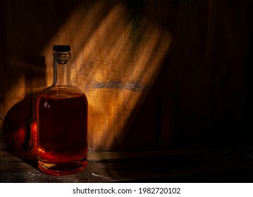 A bottle filled with a liquid of crimson color, closed with a cork on the background of old wooden walls, illuminated by the sun's rays