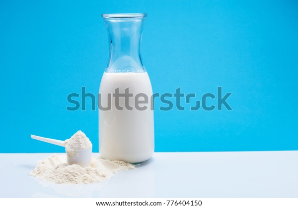 Bottle of fresh milk with powdered\
milk and spoon for baby on white table,blue\
background