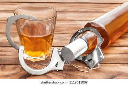 Bottle And Glass With Alcohol Drink And Handcuffs On Wooden Table. Alcohol Dependence.