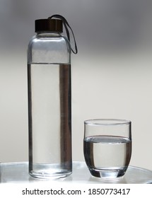 bottle and a glass filled with water on illuminated gray background. Healthy life concept.