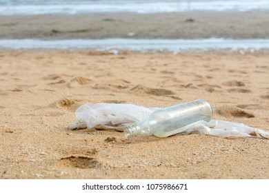 Bottle glass and plastic bag are on the beach leave by tourist - Shutterstock ID 1075986671
