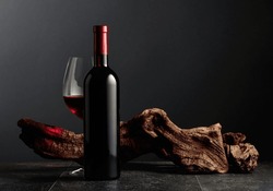 Bottle And Glass Of Red Wine On A Black Stone Table. In The Background Old Weathered Snag. Frontal View With Copy Space.