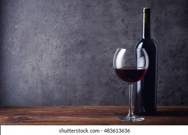 Bottle and glass of red wine on dark background
