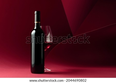 Bottle and glass of red wine on a red background. Copy space for your text.