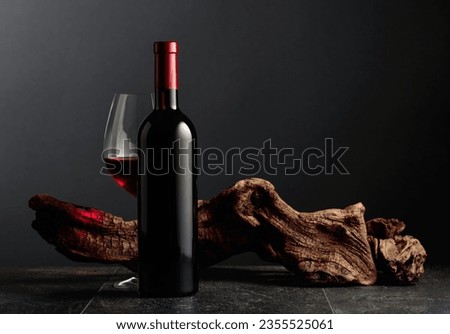 Bottle and glass of red wine on a black stone table. In the background old weathered snag. Frontal view with copy space.