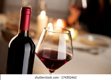 Bottle and glass of red wine with restaurant on background.
