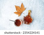 Bottle and glass of tasty maple syrup on grey background