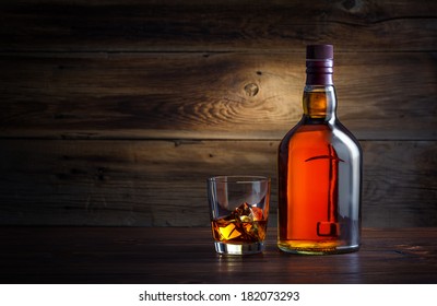 bottle and glass of whiskey with ice on a wooden background