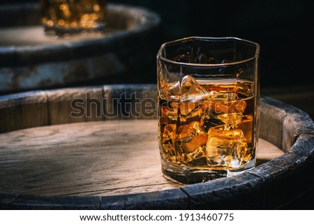 Bottle and glass of whiskey with ice on a wooden background. Glass of Scotch whiskey and ice sits on top of a rustic whiskey barrel. Whiskey with ice.