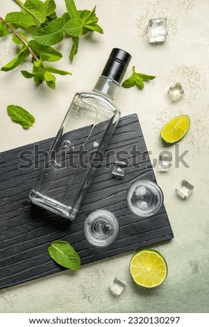 Bottle and glasses of vodka with lime on light background