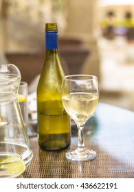 Bottle Of Half Empty Chilled White Wine Alcohol On A Wicker Table With A Full Glass And Jug Of Water