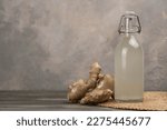 Bottle with homemade ginger ale, lemon and gingerroot on gray background. Front view.