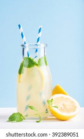 Bottle of homemade lemonade with mint, ice and lemons, paper straws and pastel blue background, selective focus