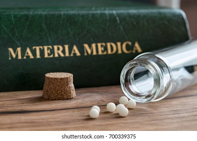 A bottle of homeopathic globules with a homeopathic materia medica in the background
