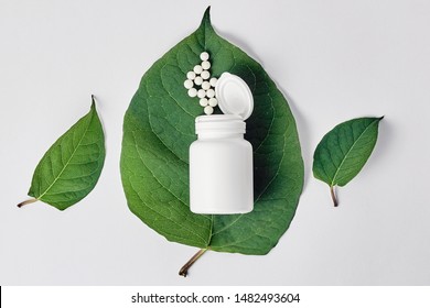 Bottle with homeopathic pills on green plant leaf. Homeopathy, naturopathy and alternative herbal medicine. Top view, flat lay over white background