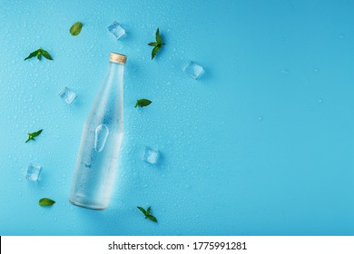 A bottle ice water  ice cubes  drops   mint leaves blue background 