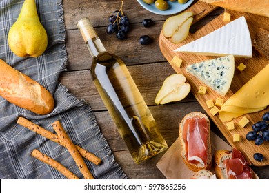 Bottle And Ingredients For Meal. Baguette, Bread Sticks And Pear On Table Napkin, A Cutting Board With Cheeses, Fruits And Jamon Toasts. Cooking A Dinner In French Style For A Date.