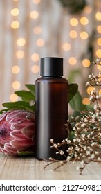 A Bottle Of Liquid Cosmetics On The Table In Flowers On A Background Of Bokeh, Close-up. Beauty Concept, Mockup. Vertical Orientation, Copy Space, No People