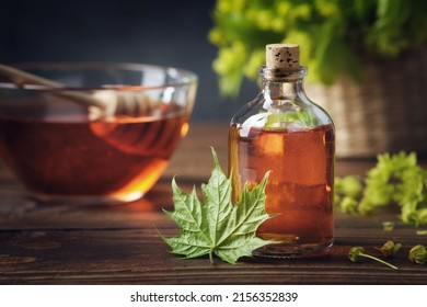 Bottle of maple syrup or healthy tincture and spring maple leaf. Bowl of maple syrup and wooden dipper on background.
