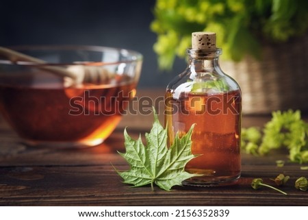 Bottle of maple syrup or healthy tincture and spring maple leaf. Bowl of maple syrup and wooden dipper on background.