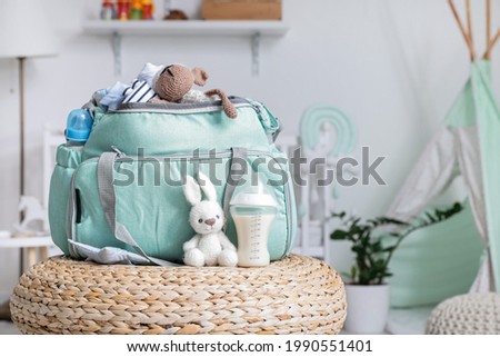 Bottle of milk for baby and bag with toys on ottoman at home