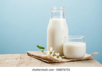 A bottle of milk and glass of milk on a wooden table on a blue background
