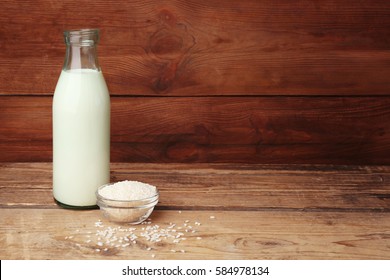 Bottle of milk and little bowl with rice on wooden background