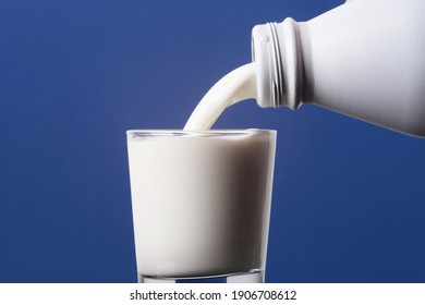 Bouteille de lait se déversant dans un verre au bord et isolée sur fond bleu