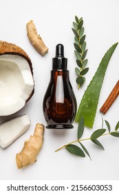 Bottle Of Natural Serum With Coconut, Ginger, Plant Leaves And Cinnamon On White Background