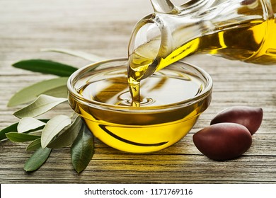 Bottle of Olive oil pouring in a glass bowl with olives and branch