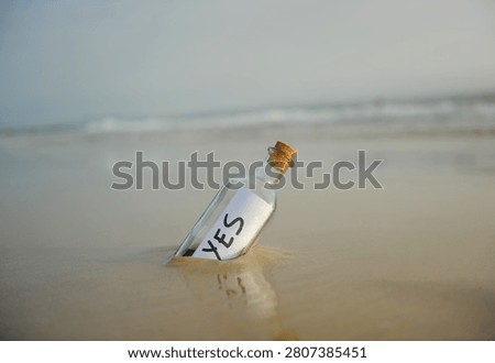 Bottle on the beach with an affirmative answer inside, yes, positive message. Affirmative response sent. Misty beach landscape background with gentle waves