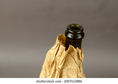 Bottle In A Paper Bag On A Gray Background. Dark Bottle Of Alcohol In A Crumpled Brown Bag. Close-up. Selective Focus.