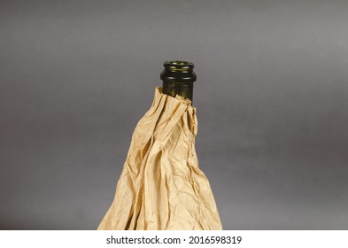 Bottle In A Paper Bag On A Gray Background. Dark Bottle Of Alcohol In A Crumpled Brown Bag. Close-up. Selective Focus.