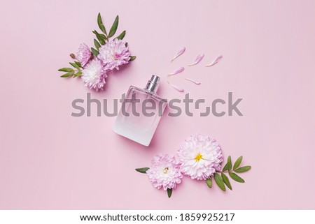 A bottle of perfume, flowers and petals on pink background. Floral fragrance, creative flat lay composition