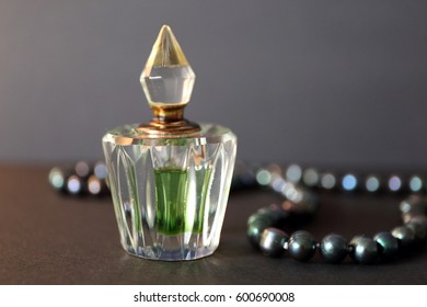 A bottle of perfume and a gray pearl necklace on a black background