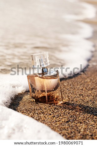 A bottle of perfume on the seashore is enveloped in a wave. Yellow sand on the beach, marine cosmetics and fragrance.